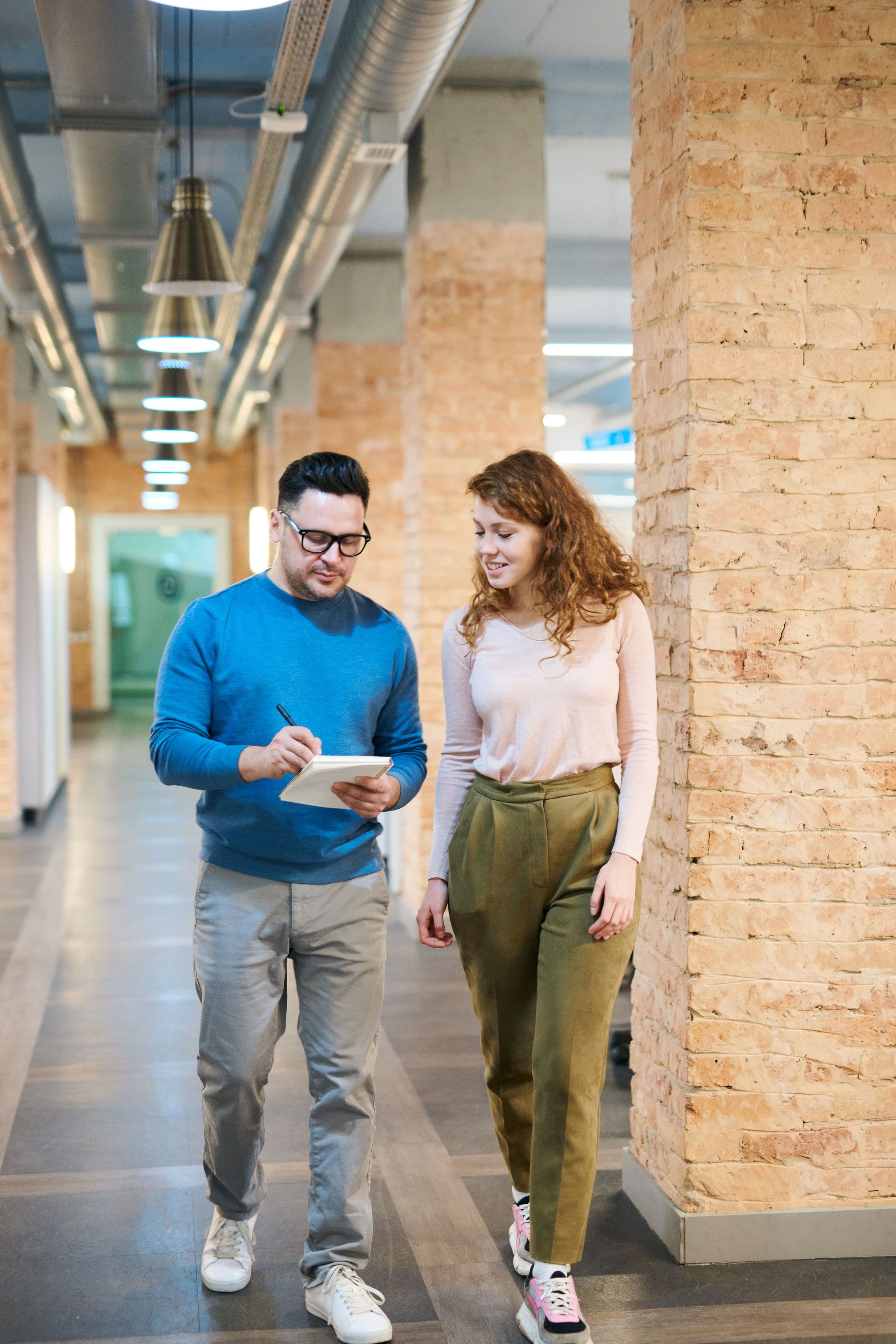 Two colleagues reviewing notes while walking through an office corridor